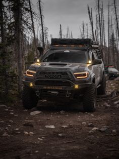 two trucks driving down a dirt road in the woods