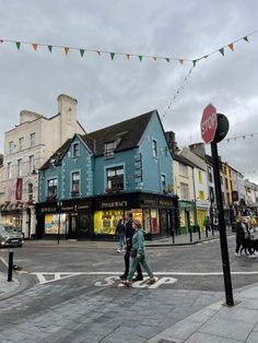 two people crossing the street in front of shops