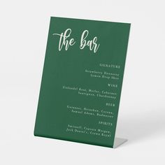 a green menu card with the word the bar written on it in white ink, against a plain background