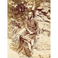 an old photo of a native american man sitting on a rock with his headdress