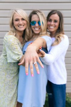 three women standing next to each other with their arms around one another, both smiling and pointing at the camera