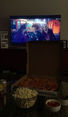 an open box with popcorn and other food on the table in front of a flat screen tv