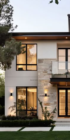 a modern house with large windows and lots of lights on the front porch, along with an outdoor dining area