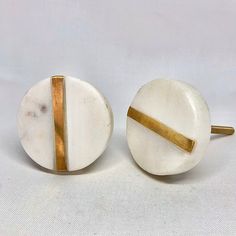 two white marble knobs with gold lines on them, one is round and the other is oval