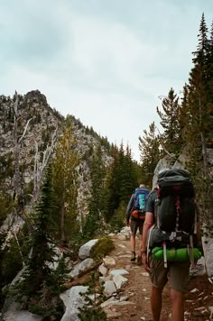 three people hiking up a mountain trail in the mountains with backpacks on their backs