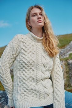 a woman sitting on top of a rock wearing a white cable knit sweater and jeans