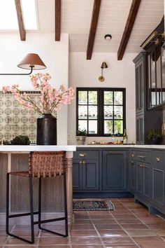 a kitchen with blue cabinets and white counter tops, brown tile flooring and wooden beams