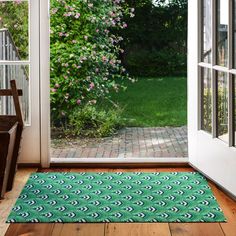 an open door with a green rug on the floor and pink flowers in the background