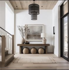 an entryway with white walls and wood flooring, two vases on the table