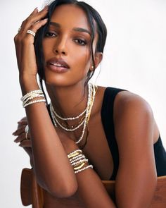 a woman sitting in a chair with her hand on her head and pearls around her neck