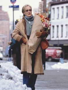 a woman is walking down the street with a large bag on her back and flowers in her hand