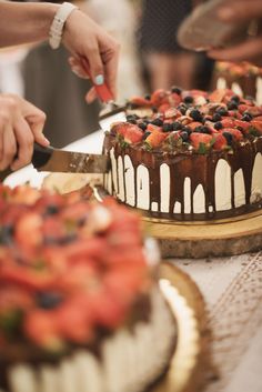 two people are cutting into a cake with chocolate and strawberries on the top one