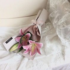 a bouquet of pink flowers sitting on top of a white bed next to a pillow