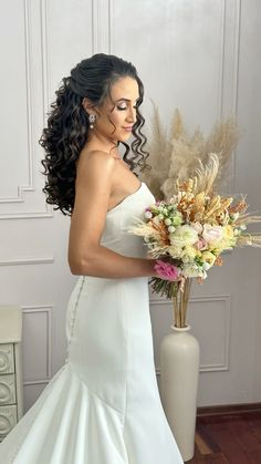 a woman in a white wedding dress holding a large flower bouquet and looking at the camera