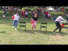 some people are playing frisbee in the grass with chairs and red ballons