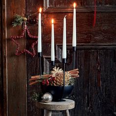 three candles are lit in a black bowl with cinnamons and pine cones on it