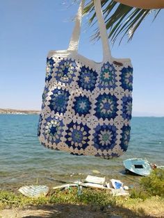 a crocheted tote bag hanging from a palm tree next to the ocean