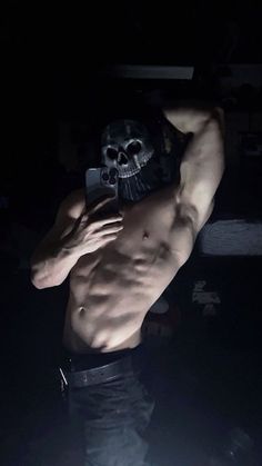 a shirtless man wearing a mask and holding a cell phone to his face in the dark