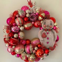 a christmas wreath with ornaments hanging on the wall and a stuffed animal in the middle