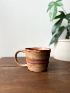 a coffee cup sitting on top of a wooden table next to a potted plant