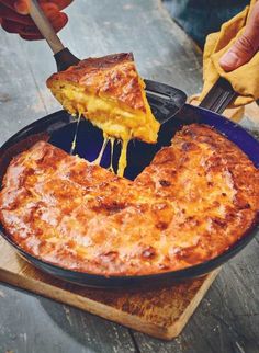 a person is taking a slice of cheesy pizza out of a skillet