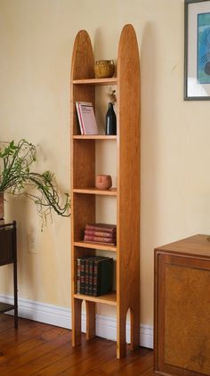 a wooden book shelf with books on it in a living room next to a plant