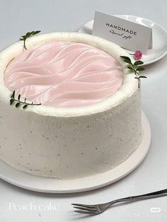 a white cake with pink frosting and green leaves on top, sitting on a plate next to a fork