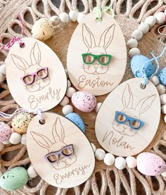 four wooden easter tags with bunny ears and glasses on them sitting on a table next to eggs