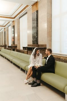 a bride and groom sitting on a green bench in the middle of a lobby area