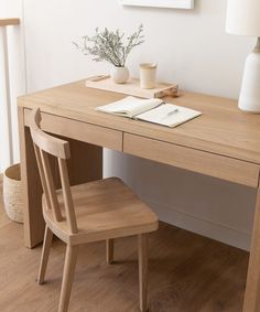 a wooden desk with two chairs and a book on it, next to a lamp