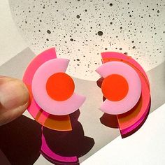 "Deconstruct your style with these modern geometric studs. A modern take on the Art Deco aesthetic, these abstracted eyes in a concentric arrangement will add color blocking to your outfit. Bold with a neon pink/orange backing, these earrings project a bright light effect that is sure to make a statement. Made from 1/8\" thick acrylic, these earrings are made of solid construction with a mixture of solid and clear acrylic pieces that let light through. Each earring measures approximately 1-3/8 i Bold Geometric Earrings With Bold Design, Bold Geometric Designed Earrings, Pink Geometric Earrings, Modern Multicolor Earrings With Bold Design, Bold Geometric Earrings, Modern Handmade Geometric Earrings, Handmade Modern Geometric Earrings, Modern Geometric Earrings, Bold Handmade Geometric Earrings