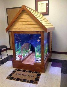 a small wooden house sitting on top of a tiled floor next to a window with fish in it