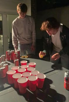 two young men standing at a table with cups on it