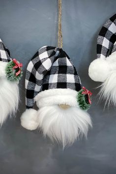 three christmas hats hanging from strings on a gray background with white fur and green pom - poms