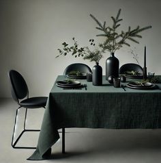 the table is set with black plates and green napkins on it, along with two vases filled with greenery