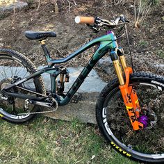 an orange and blue mountain bike parked on the side of a rock path next to some grass