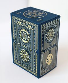 a blue and gold playing card box on a white surface with an intricate design in the middle