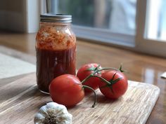 tomatoes and garlic on a cutting board next to a jar of tomato sauce