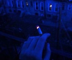 a hand holding a lit up bottle in front of a building at night with the light on