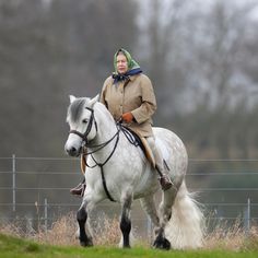 a woman riding on the back of a white horse in a field next to a fence