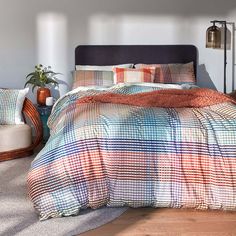 a bed with plaid comforter and pillows on top of it in a room next to a chair