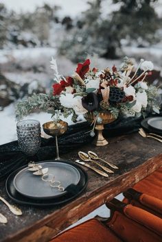 the table is set with black plates and gold utensils, silverware, and flowers