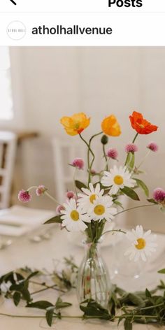 a vase filled with lots of flowers on top of a white table covered in greenery