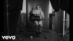 a man sitting on top of a chair holding a guitar in front of his face