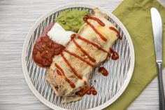 an enchilada on a plate with guacamole and sour cream