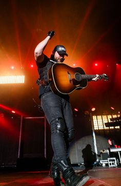 a man on stage with his guitar in the air and red lights behind him,