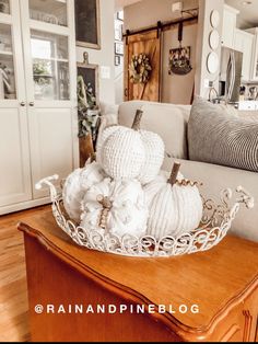 white pumpkins are sitting in a basket on a table next to a couch and pillows