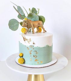 a cake decorated with gold and blue frosting on top of a white plate next to a green leafy plant