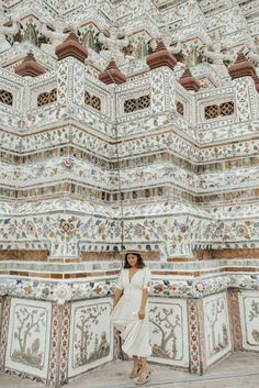 a woman wearing a white dress and hat standing in front of an intricately painted building