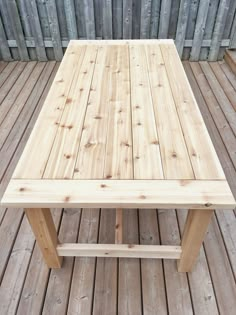 a square wooden table sitting on top of a wooden deck next to a wood fence